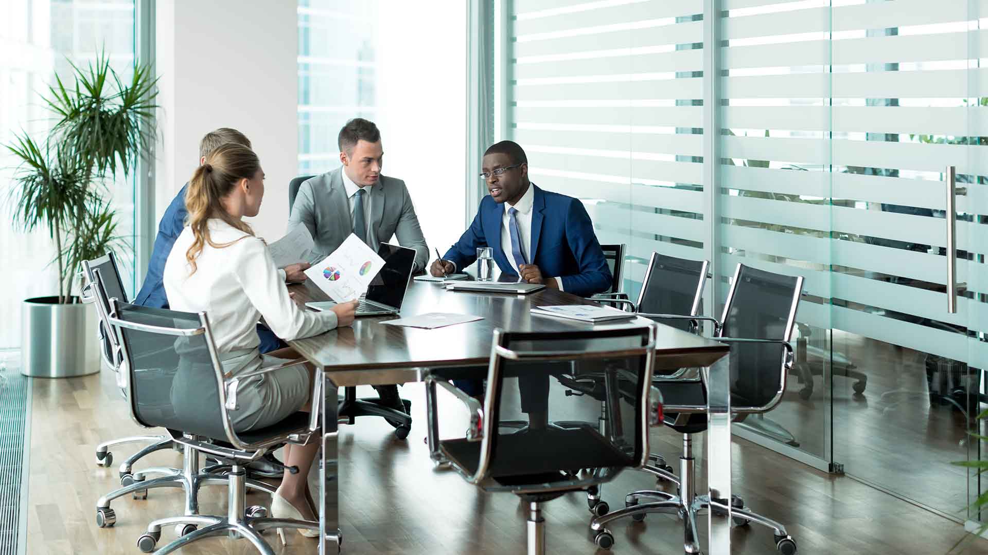 Business team meeting around a conference table in a glass-walled boardroom