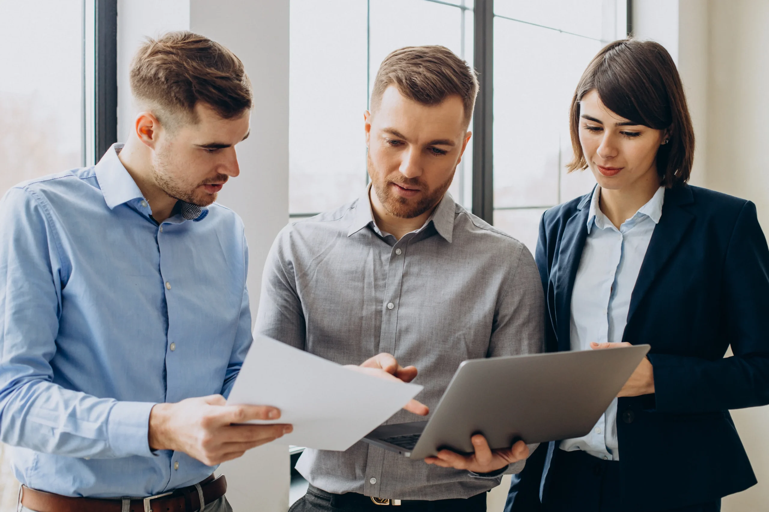 Three colleagues reviewing documents and a tablet together in an office