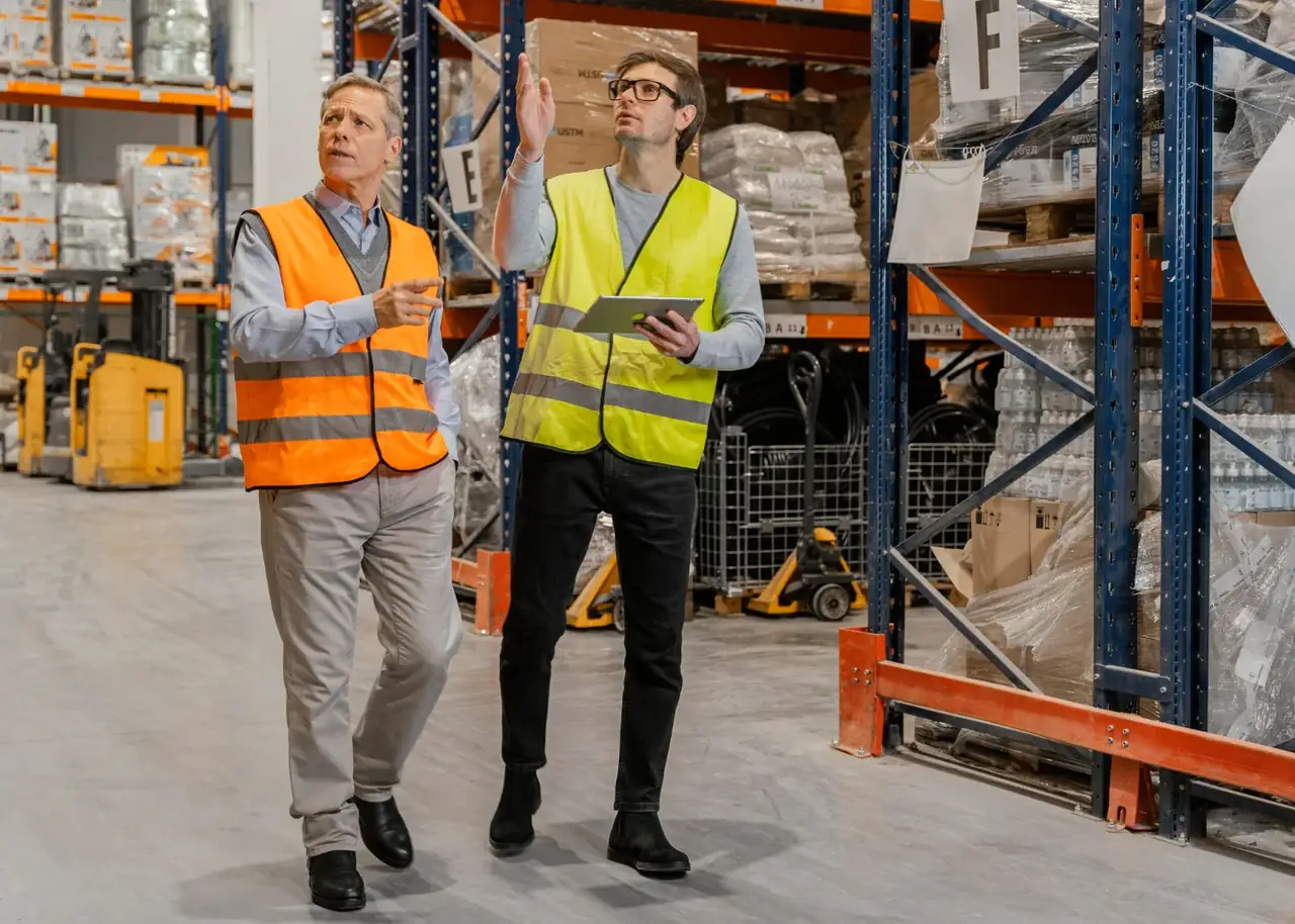 Warehouse workers in high-visibility vests walking between racks of stored inventory